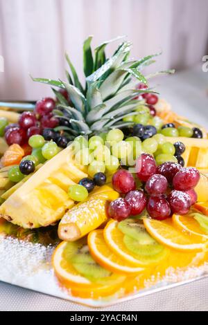 Piatto di frutta colorato con ananas, uva, arance e kiwi in un ambiente vivace Foto Stock