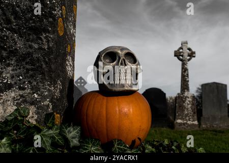 Oscura carta da parati di halloween con teschio umano e zucca nel cimitero, giorno di tutti i santi, lapidi celtiche a croce Foto Stock