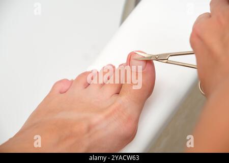 Primo piano dell'unghia del piede rifilata con piccole forbici. Concetto di igiene e cura personale Foto Stock