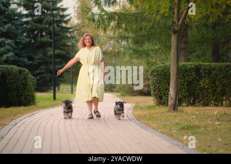 Una donna di 50 anni cammina con i suoi due schnauzer zwerg nel parco, apprezzando l'esperienza all'aria aperta. Foto Stock