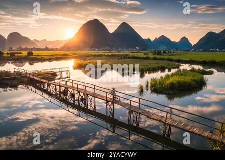 La scena rurale del tramonto risplende sulla montagna con un abitante che spinge la bicicletta su un ponte di legno sul fiume nella campagna di Bac Son Valley, Lang Son, V Foto Stock