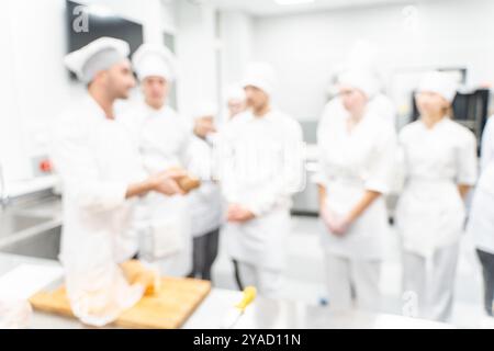 Sfondo sfocato: Un insegnante di cucina o uno chef conduce una master class sulla preparazione del pane per i suoi studenti nel laboratorio di produzione. Foto di alta qualità Foto Stock