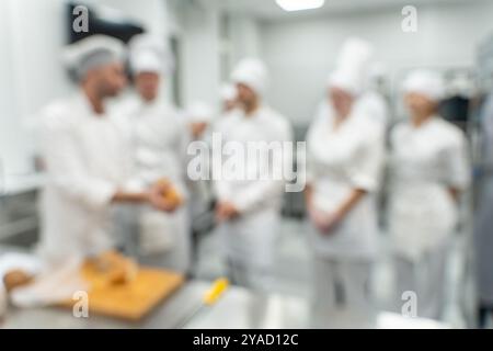 Sfondo sfocato: Un insegnante di cucina o uno chef conduce una master class sulla preparazione del pane per i suoi studenti nel laboratorio di produzione. Foto di alta qualità Foto Stock