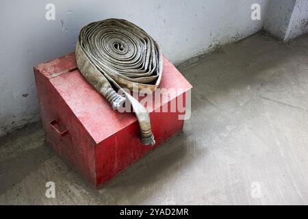 Manichetta antincendio vecchia condizione sbiadita su una scatola antincendio rossa con sabbia all'interno di un edificio industriale con pavimento in cemento focalizzazione selettiva con spazio imbottito. Foto Stock