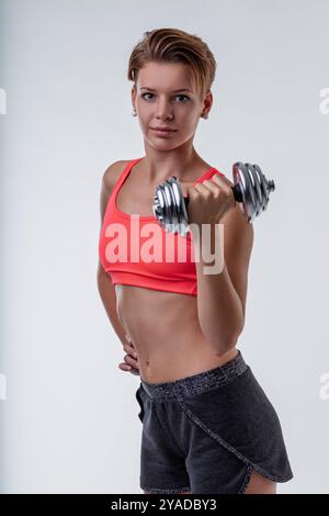 Una giovane donna determinata solleva un manubrio in una palestra, mostrando forza e fiducia nella sua routine di fitness Foto Stock