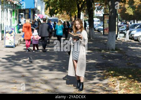 Romny, Ucraina, 29 settembre 2019: Una giovane donna sta per strada e legge un libro. Foto Stock