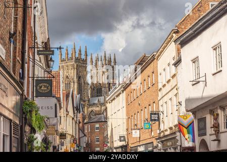 Storica strada della città fiancheggiata da negozi e dalle torri di una cattedrale che si innalzano sopra i tetti. Un cielo con nuvole è sopra. Foto Stock