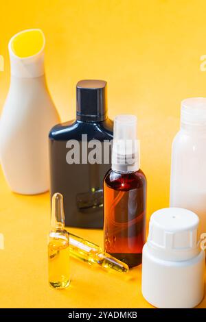 Una collezione di vari contenitori di prodotti cosmetici e per la cura della pelle su un vivace sfondo giallo. La disposizione include flaconi spray, fiale, e. Foto Stock