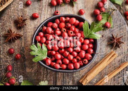 Bacche di biancospino selvatico raccolte in autunno in una ciotola nera su un tavolo di legno, vista dall'alto Foto Stock