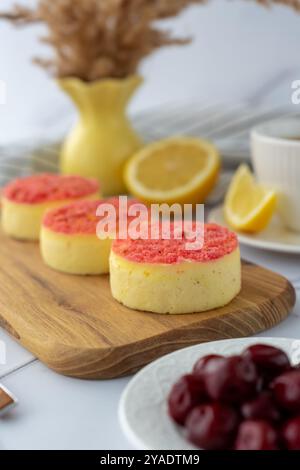 Mini cheesecake con copertura crumble rosa serviti su un tavolo di legno con limoni e ciliegie. Concetto di dessert estivo, sapori freschi e artigianali Foto Stock