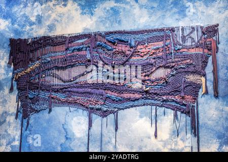 Vista dettagliata dell'arte tessile intrecciata appesa su una parete con trama blu. Foto Stock