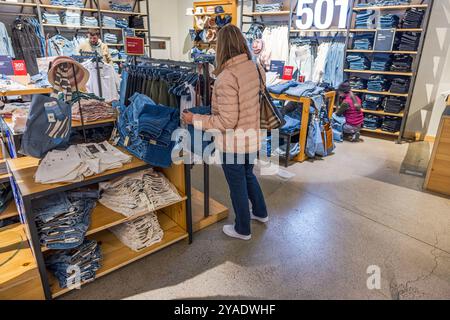 Donna che sfoggia pantaloncini e jeans in denim nel negozio Levi's con scaffali e scaffali pieni di abbigliamento. New York. STATI UNITI. Foto Stock