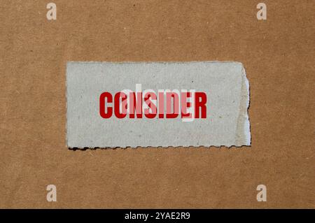 Considerare il messaggio scritto su un pezzo di carta strappato con sfondo di cartone. Simbolo concettuale da considerare. Copia spazio. Foto Stock