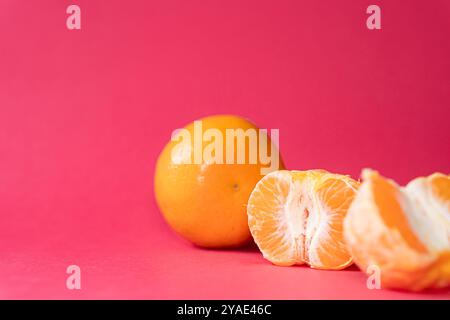 Due arance su un vivace sfondo rosa, una arancia parzialmente sbucciata, che mostra il suo interno succoso. I colori brillanti creano un contrasto sorprendente, Foto Stock