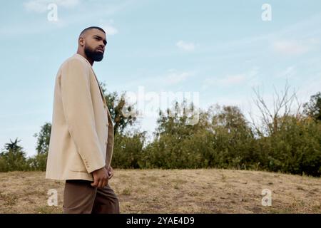 Vestito con abiti alla moda in autunno, un uomo cammina con grazia attraverso un tranquillo paesaggio circondato dalla natura. Foto Stock