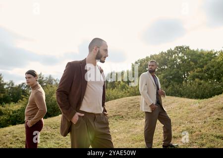 Tre uomini vestiti eleganti si mettono in posa in un campo autunnale sotto la luce calda e soffusa del sole. Foto Stock