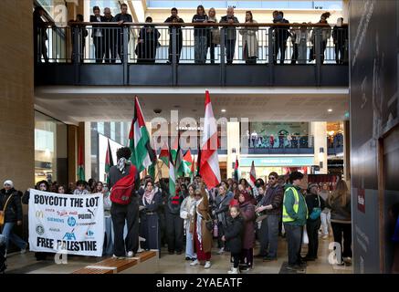 Cambridge, Inghilterra, Regno Unito. 13 ottobre 2024. I manifestanti, molti studenti universitari, ascoltano gli oratori del centro commerciale Grand Arcade, osservati dai membri del pubblico dal piano superiore. I manifestanti si radunano attraverso il centro di Cambridge chiedendo che l'università e il pubblico in generale cedano e boicottino le aziende che sostengono gli israeliani nella loro guerra contro Gaza, Libano e Cisgiordania. (Credit Image: © Martin Pope/ZUMA Press Wire) SOLO PER USO EDITORIALE! Non per USO commerciale! Foto Stock