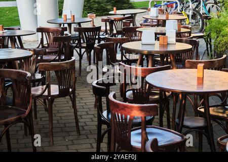 Una terrazza all'aperto vuota con tavoli e sedie in legno d'epoca disposti in modo ordinato, in attesa dei clienti in una giornata di sole, con un accogliente e accogliente Foto Stock