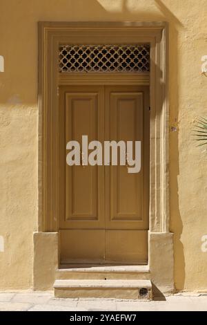 Gelbe beige Holztür. porta in legno di colore giallo beige. Türklopfer. bussano alla porta. oro. nobel. muro giallo. gelbe Wand. Mdina. Malta. glänzend. Eisengitter. Foto Stock