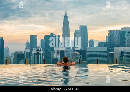 Uomo turista che si rilassa nella piscina a sfioro sul tetto all'alba, Kuala Lumpur, Malesia. Viaggiatore di sesso maschile che gode di vista sulla città con servizi finanziari del centro Foto Stock