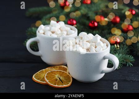 Gustose bevande a base di cioccolata calda con marshmallow in tazze e fette di arancia asciutta su un tavolo di legno nero, primo piano Foto Stock