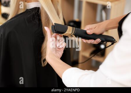 Parrucchiere arriccia i capelli della donna con il ferro da stiro nel salone, primo piano Foto Stock