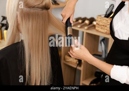 Parrucchiere arriccia i capelli della donna con il ferro da stiro nel salone, primo piano Foto Stock