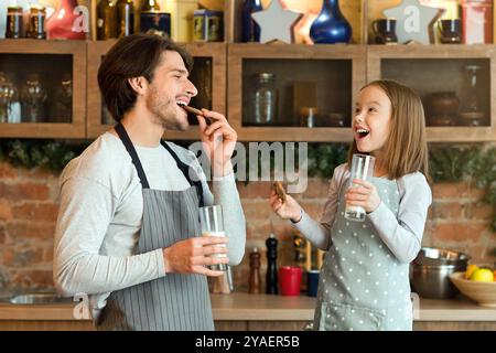 Papà allegro e figlia piccola mangiare biscotti e bere latte in cucina Foto Stock