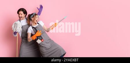 Coppia di janitors che si divertono durante la pulizia, ingannando con mop e scopa Foto Stock