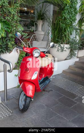 BRISBANE, QUEENSLAND, AUSTRALIA. 11 settembre 2024; Vespa rossa parcheggiata fuori da un bar decorato con foglie verdi. orientamento verticale. Foto Stock