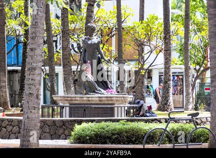 Oahu, Hawaii, USA - 26 febbraio 2024: Un senzatetto riposa alla presenza della storica statua della Principessa Kaiulani delle Hawaii come turisti benestanti Foto Stock