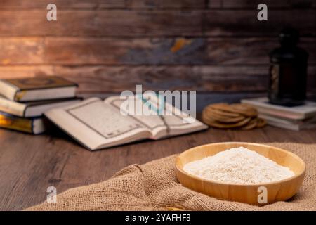 Sacro Corano e un granello di riso in una ciotola di legno nel sacco su un tavolo di legno, concetto zakat islamico. Musulmani per aiutare i poveri e i bisognosi. Concettuale S Foto Stock