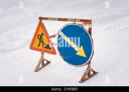 Segnali di costruzione e deviazione posizionati in un ambiente innevato che indicano i lavori stradali in corso in inverno Foto Stock