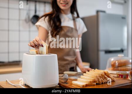 Primo piano di una donna che mette una fetta di pane in un tostapane, prepara toast in cucina, prepara la colazione. cucina casalinga, vita domestica Foto Stock