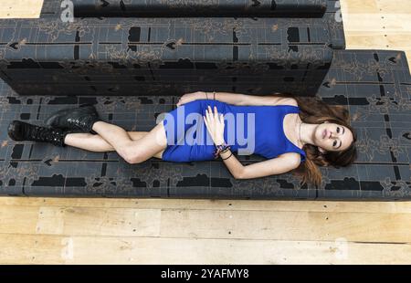 Ritratto di una donna bianca di 18 anni, in abito corto blu, distesa su un divano grigio, vista dall'alto, Bruxelles Foto Stock