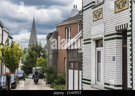 Uccle, Bruxelles, Belgio, 06 14 2019, uomo in bicicletta che sale per la curling Saint Job Street con vista sulla torre della chiesa, Europa Foto Stock