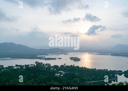 Gli ultimi raggi del sole si riflettono sul lago pichola, circondato da colline e palazzi di udaipur, india Foto Stock