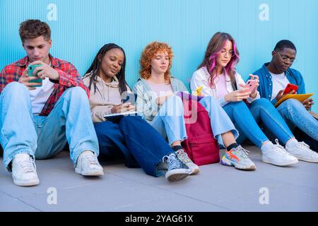 Un gruppo di giovani diversi seduti all'aperto utilizzando smartphone e notebook Foto Stock