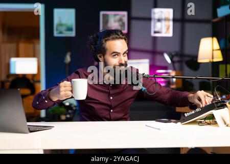 Artista ASMR che utilizza un microfono di alta qualità in studio per realizzare video anti-stress, discutendo con gli spettatori mentre beve un caffè. Uomo che utilizza un microfono professionale per registrare contenuti rilassanti Foto Stock