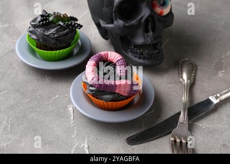 Teschio, posate e deliziosi cupcake di Halloween su sfondo grigio, primo piano Foto Stock