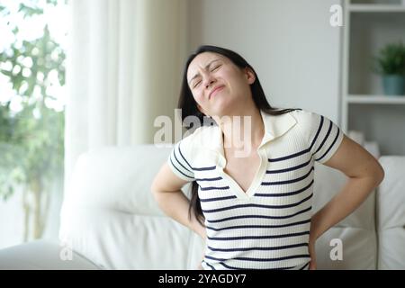 Donna asiatica che soffre lombardo seduto su un divano scomodo a casa Foto Stock