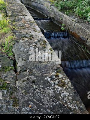 L'acqua in eccesso dal canale sopra la chiusa quattro del braccio di Rufford del canale di Leeds e Liverpool scorre intorno alla chiusa nel canale di bywash di pietra. Foto Stock