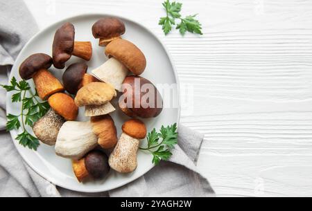 Un assortimento di funghi freschi è disposto su un piatto, mostrando forme e colori diversi, accompagnati da prezzemolo su un backgroun di legno testurizzato Foto Stock