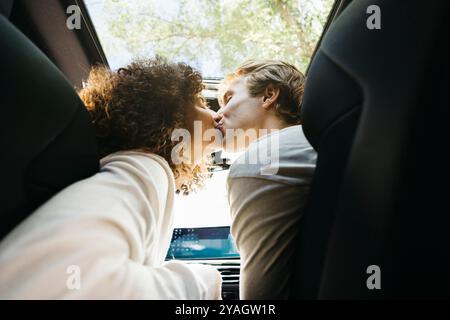 Una coppia condivide un bacio tenero all'interno della loro auto mentre si ricarica in una stazione. Enfatizzare l'amore, la sostenibilità e la tecnologia moderna. Foto Stock