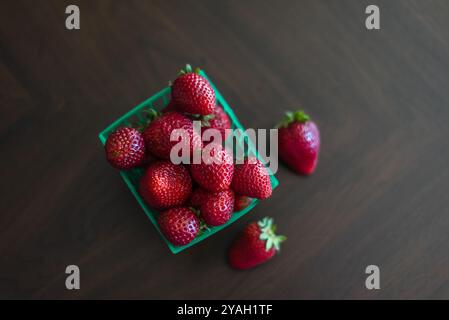 Un cestino di fragole rosse fresche su una superficie di legno scuro Foto Stock