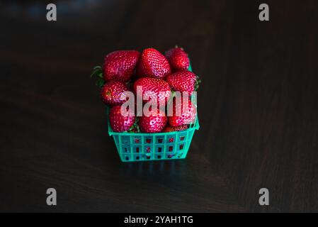 Un cestino verde pieno di fragole rosse fresche su un tavolo scuro. Foto Stock