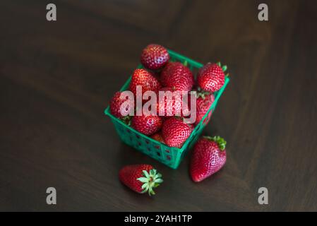 Un cestino verde pieno di fragole rosse fresche su una superficie scura. Foto Stock