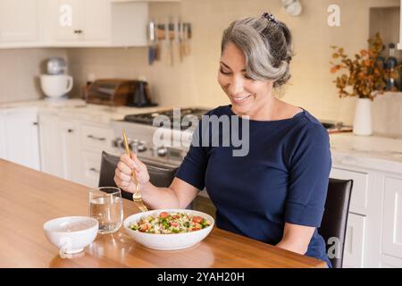 Donna che sorride alla sua Macedonia di frutta in cucina Foto Stock
