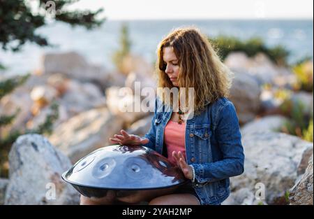 Giovane donna attraente che suona il tamburo di handpan sulla pietra Foto Stock