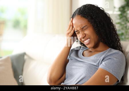 Donna nera che soffre mal di testa seduta su un divano a casa Foto Stock